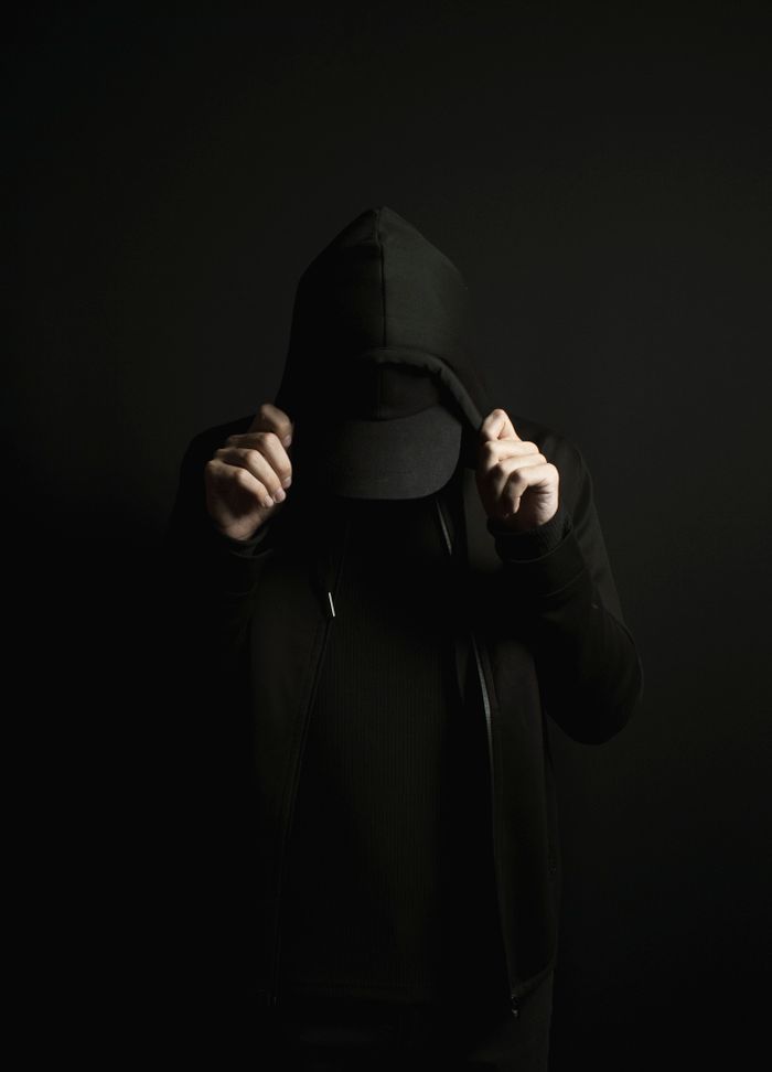 Person obscured in a dark hoodie with hands pulling the hood down, creating a mysterious look.